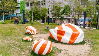 The name of this sculpture “Cam<sup>4</sup> Kau<sup>4</sup>”, is the Cantonese pronunciation of “sinking ball” (沉球), which is also the Cantonese pun for “in search of” (尋求). The sculpture symbolising fellowship and togetherness, imitates a deflated plastic ball with red and white stripes, which is inspired by the rigid plastic ball played by children in Hong Kong in the 1970s and 1980s.